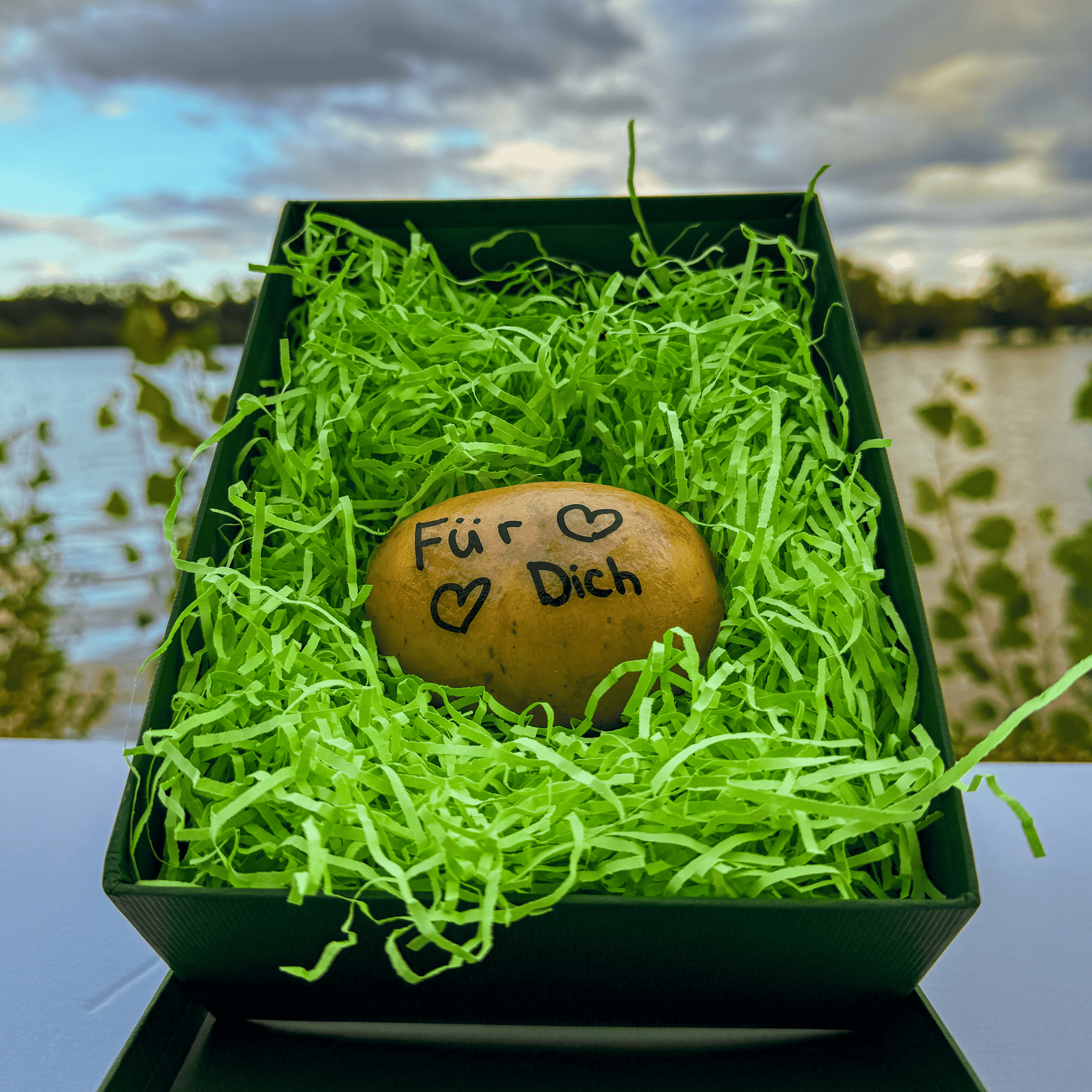 In der grünen Geschenkbox liegt eine Kartoffel. Auf der Kartoffel steht der handgeschriebene Text "Für Dich" und zwei Herzen dazu gemalt